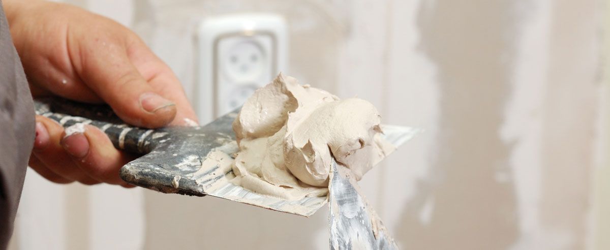Eine Hand hält eine Spachtel mit Spachtelmasse für den Trockenbau bereit